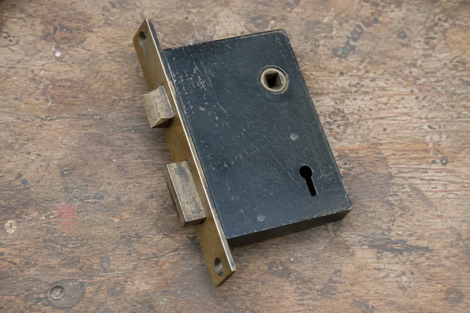 Closed mortise lock case with spindle opening, keyhole, latch and deadbolt on a wooden workbench. — Vintage Mortise Lock Service, Woodstock